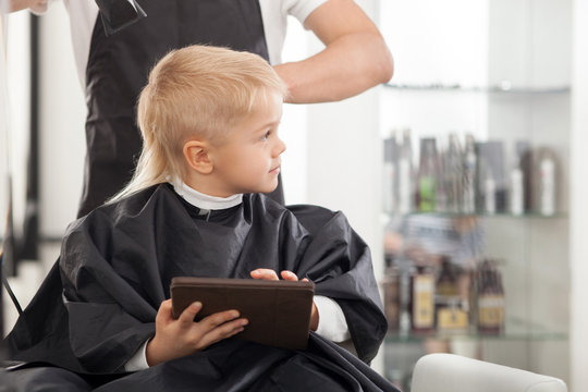 Professional young barber is making hairstyle for kid
