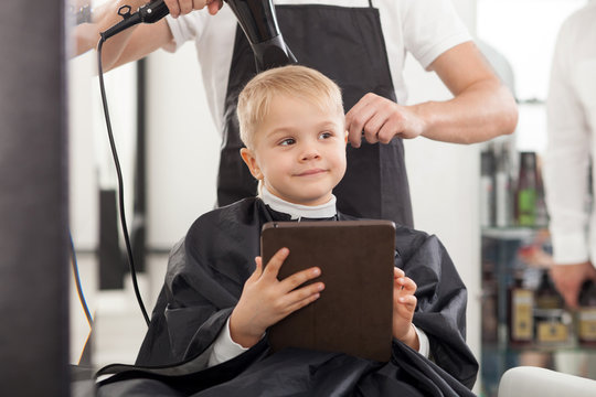 Cheerful young hairdresser is working with hair-drier