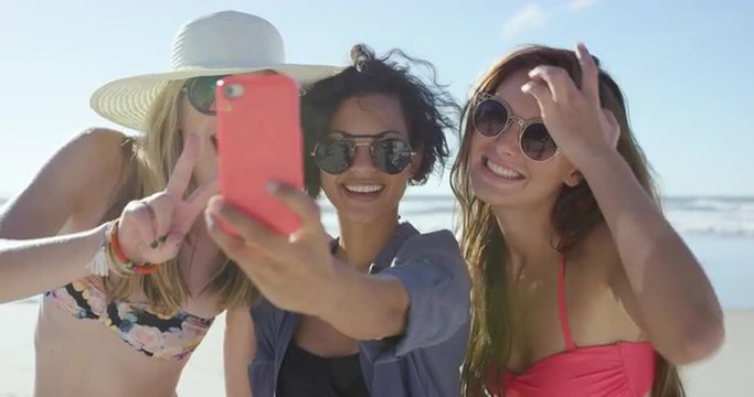 Group of girl friends taking selfies on the beach using pink phone