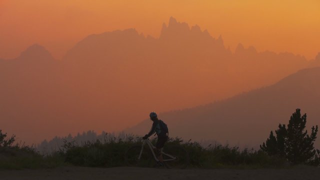 A mountain biker pulls to a stop on a hillside at sunset and takes a picture.