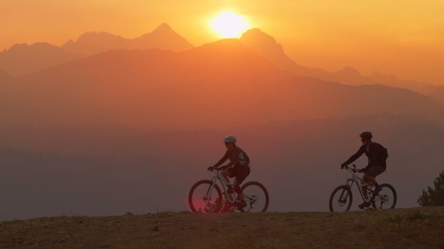 Two mountain bikers pull to a stop on a hillside at sunset.
