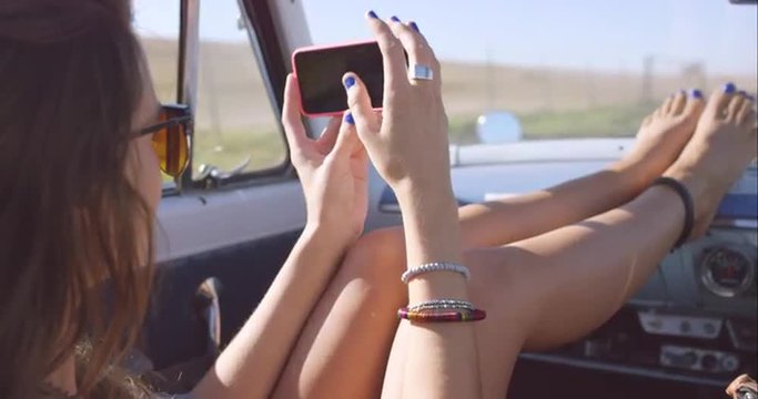 beautiful young woman taking photos with smart phone on road trip in convertible vintage car