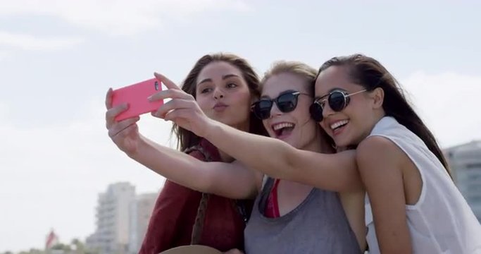 Group of teenage girls taking selfie using smartphone on vacation outdoors beach promenade