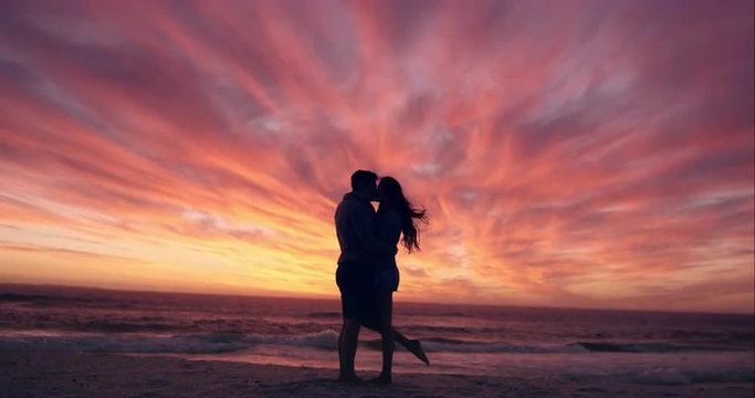 Happy couple kissing on beach at sunset silhouette in love dating on honeymoon RED DRAGON
