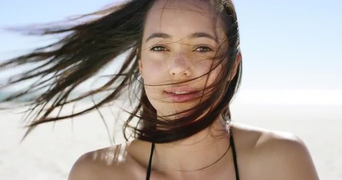 Close up portrait of beautiful young woman running hand through hair blowing in wind  on tropical beach slow motion 