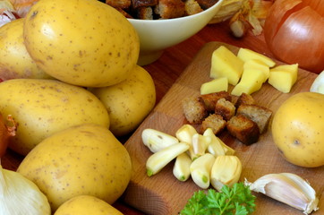Ingredients for garlic soup on chopping board - potatoes, onion, garlic, roasted bread, parsley