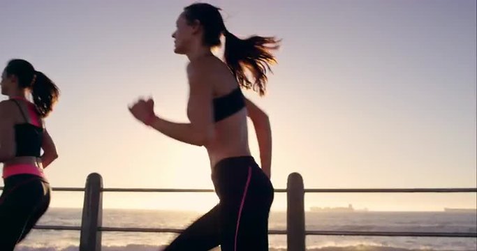 Two athletic woman running outdoors slow motion on promenade at sunset near ocean enjoying evening run
