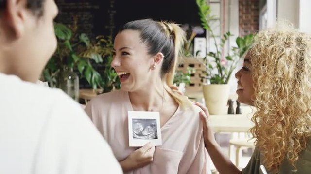 Pregnant Woman showing ultrasound picture of baby to friends celebrating