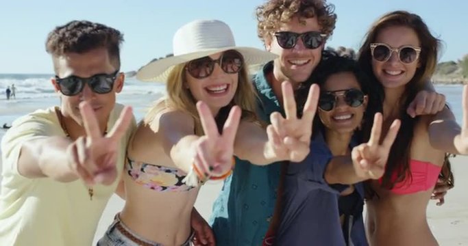 Group of friends smiling and making peace sign at camera for a portrait on the beach