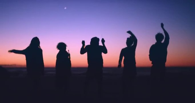 Group of friends dancing on the beach at dusk