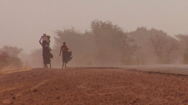 Women walk carrying goods on their heads through the Sahara desert in Mali.