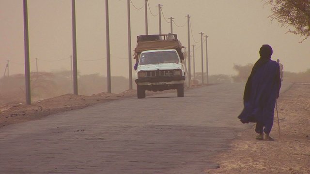 A Touareg person walks down a road through the Sahara desert in Mali during a windstorm.