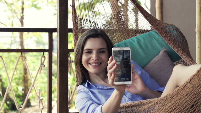 Young woman taking selfie photo with cellphone lying on hammock, slow motion 240fps