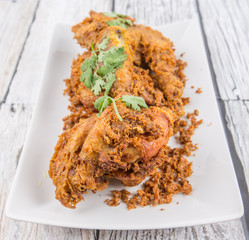 Popular Javanese dish Ayam Penyet or crispy fried chicken in a white plate over wooden background