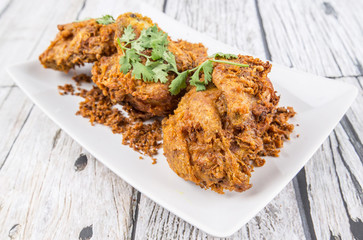 Popular Javanese dish Ayam Penyet or crispy fried chicken in a white plate over wooden background