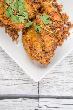 Popular Javanese dish Ayam Penyet or crispy fried chicken in a white plate over wooden background