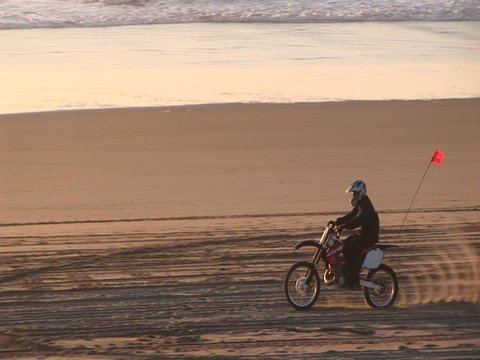 A dirt biker makes tracks on a sandy beach during the golden-hour.