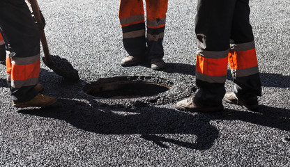 Asphalting in progress, workers near sewer manhole