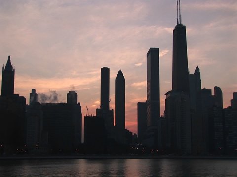 A golden-hour Chicago skyline with silhouetted buildings against a pink and orange sky.