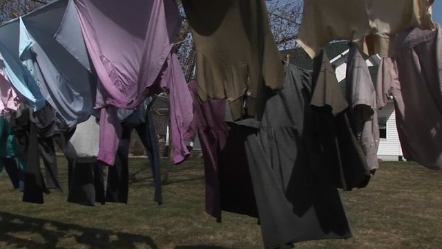Colorful shirts and dark dresses hang on a clothesline to dry in wind.