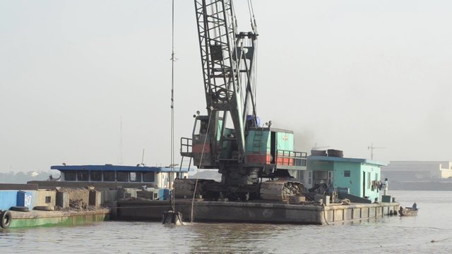 DREDGING RIVER: Wider shot crane scoops sand from river in giant bucket; from StockFootageWorld