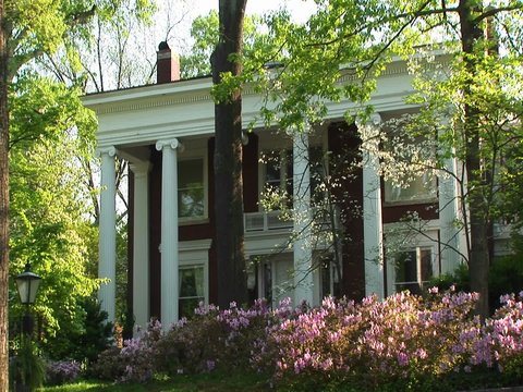 A medium-shot of an old, but well kept, country home surrounded by trees and bushes.