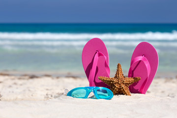Pink flip flops, swimming glasses and starfish on white sandy be