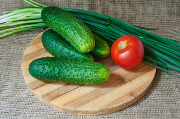 Fresh red tomatoes and cucumbers, green onions on a wooden tray