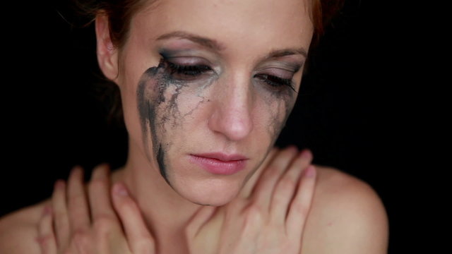 Crying woman with messy make up on face looking at the camera.