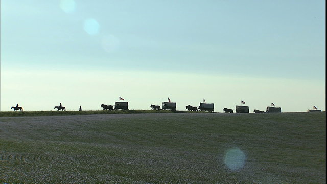 WS wagon train, back lit, crossing horizon