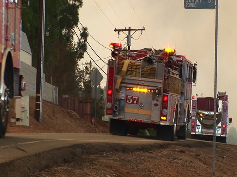 Medium shot of fire trucks racing down a street toward a wildfire.
