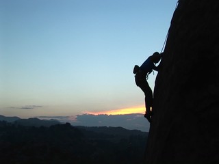 Long-shot of a rock climber scaling a cliff silhouetted against a golden-hour-sky.