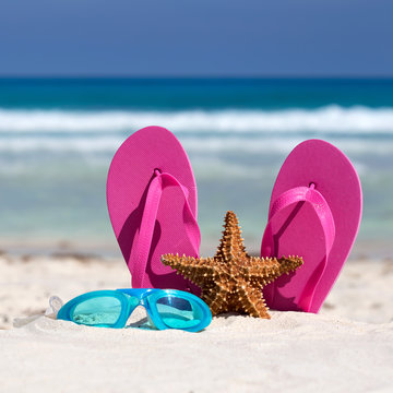 Pink flip flops, swimming glasses and starfish on white sandy be