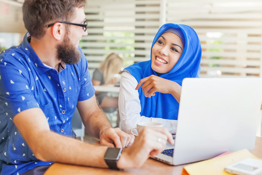 Asian Muslim Woman And Caucasian Man Looking At Screen Of Laptop