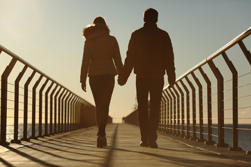 Back silhouette of a couple walking holding hands © Antonioguillem