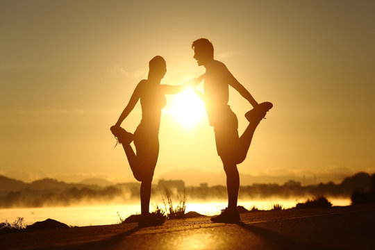 Silhouette of a fitness couple stretching at sunset