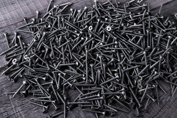 Pile of black screws on wooden background