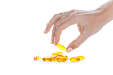 Soft gels pills with Omega-3 oil in fingers closeup on white