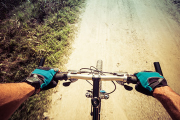 Closeup on hands and handlerbar of a man riding on a dirty road on a mountain bike