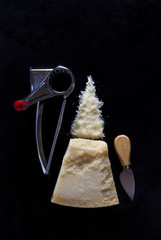 a piece of Parmesan cheese on dark with a manual cheese grater a