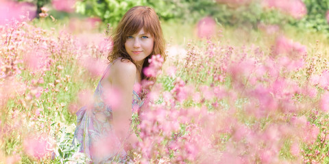 Pretty young woman is sitting in the field surrounded by flowers. - 91711005