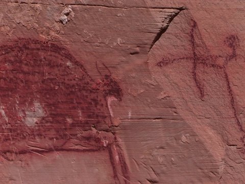 A slow pan across mysterious petroglyphs in the Southwest desert of the USA showing early man killing or hunting with a bow and arrow.