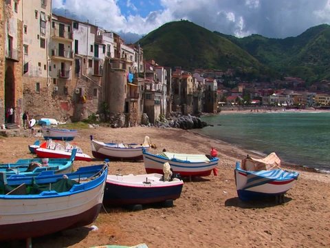 Boats on a beach next to the ocean and houses in Cefalu, Italy.  