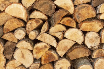 Fototapeta premium Background of stacked wood. Ready firewood. Various kinds of wooden logs stacked on top of each other. Stack of wood, firewood, background. Dry chopped firewood logs ready for winter. 