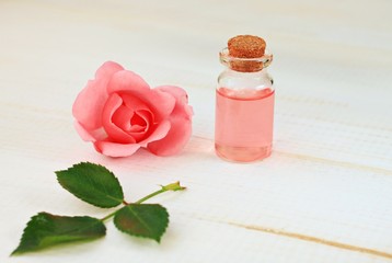 Fresh sensual rose attar in cosmetic bottle, light wooden backdrop empty space