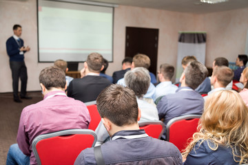 Speaker on the podium. People at conference hall, rear view