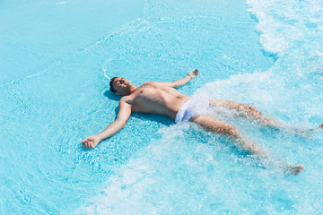 Young Man Lying on Back in Shallow Waves of Pool