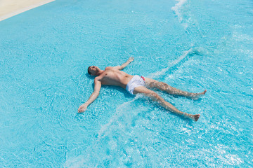 Young Man Lying on Back in Shallow Waves of Pool