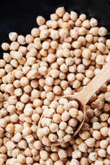 Closeup chickpea in wooden spoon and heap chickpea scattered on the black background, top view