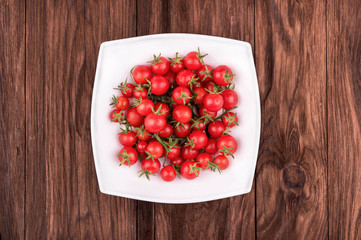 White bowl with fresh small red cherry tomatoes on a wooden background a top view